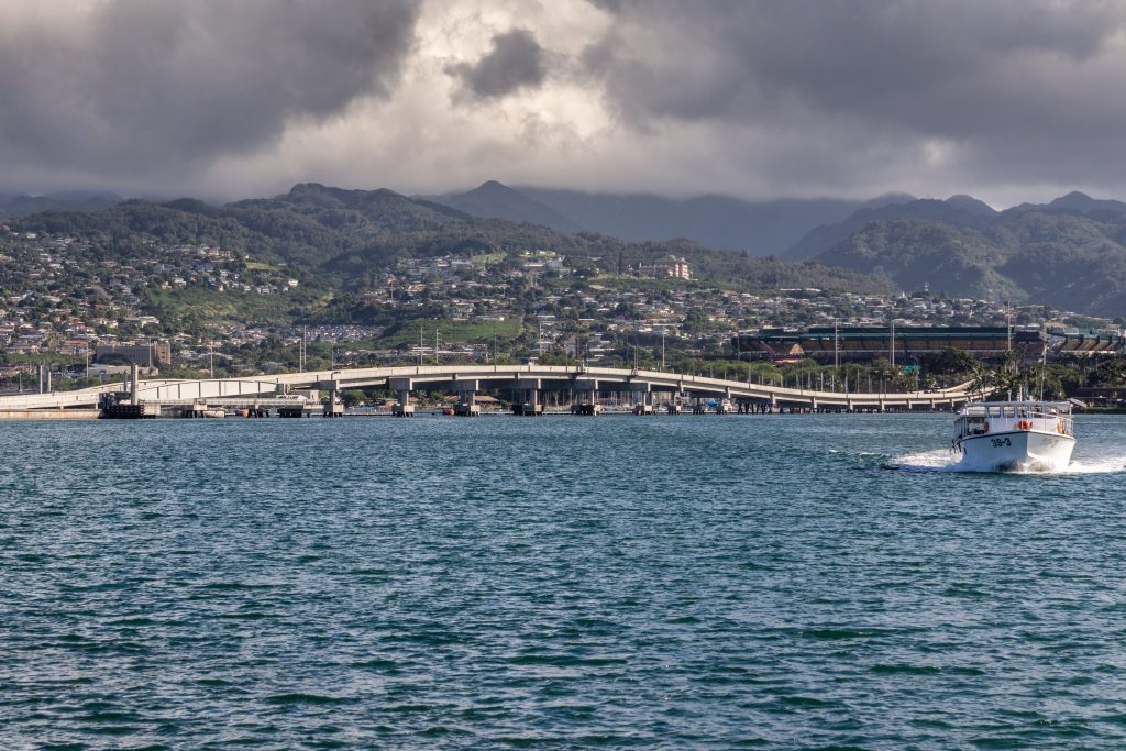 Pearl Harbor bridge framed by palm trees and ocean under cloudy skies
