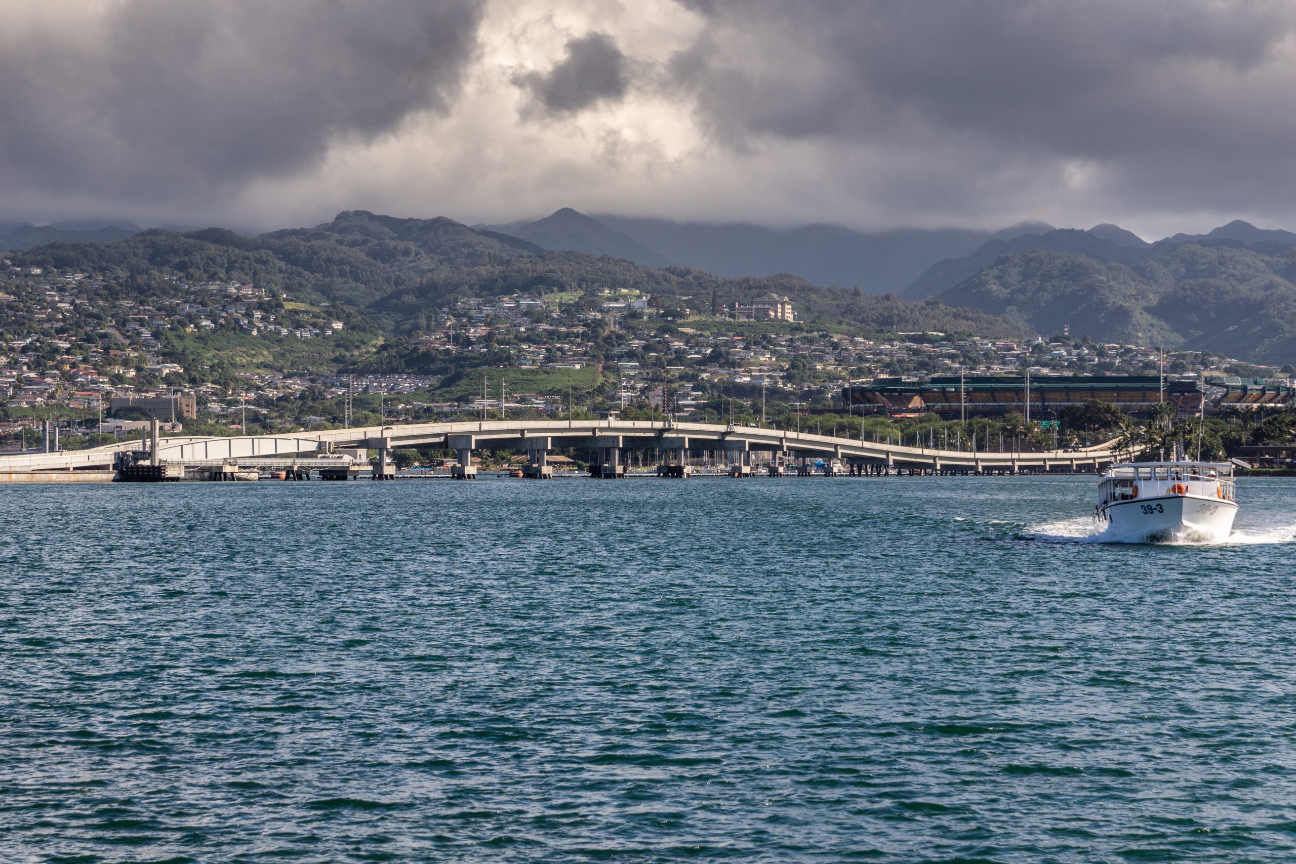 Pearl Harbor bridge framed by palm trees and ocean under cloudy skies