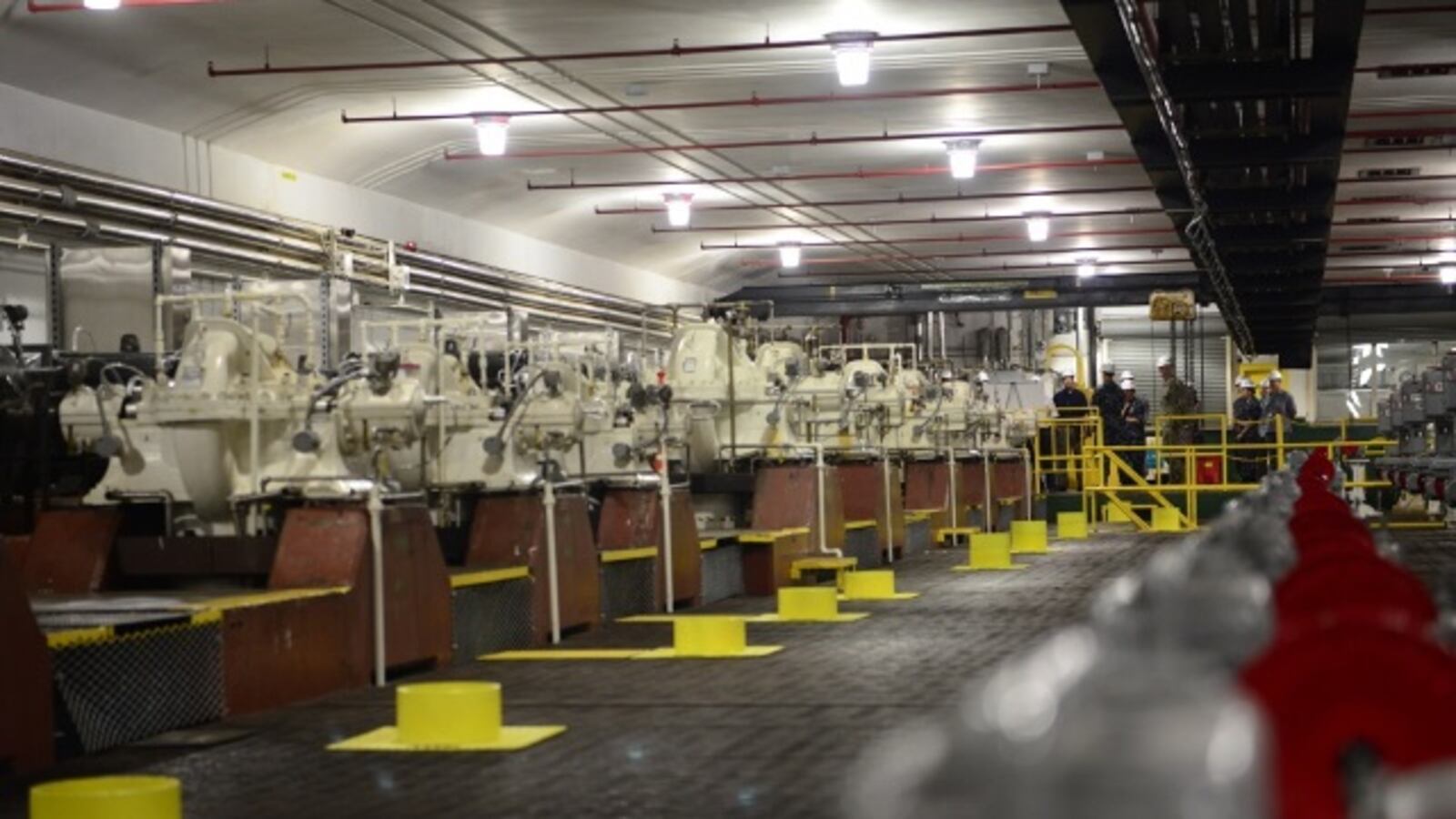 Rows of large industrial pumps in a facility; workers visible in the background. Red Hill Registry project.