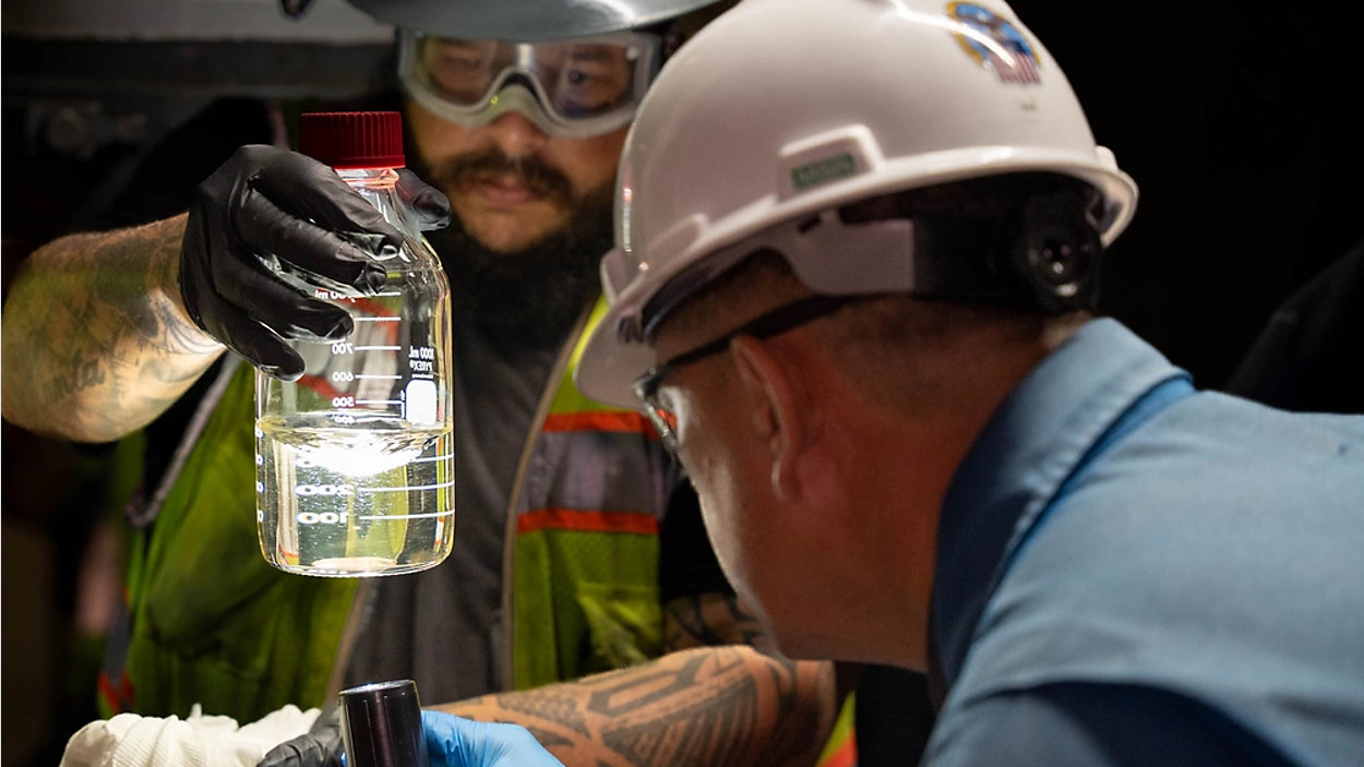 Two technicians examine a sample in a glass beaker, part of the Red Hill health registry.