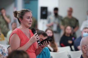 Woman speaking at a microphone, explaining the Red Hill Registry.