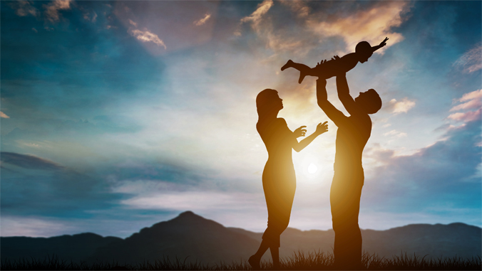 Silhouette of a happy family at sunset. Parents joyfully toss their child in the air.