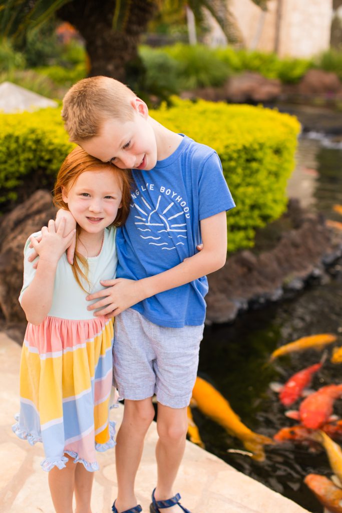 Siblings hugging near a koi pond in a lush, tropical Hawaiian garden